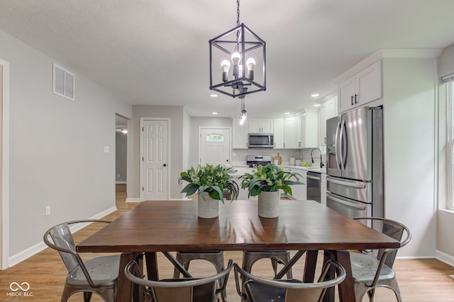 dining space featuring sink, an inviting chandelier, and light hardwood / wood-style floors