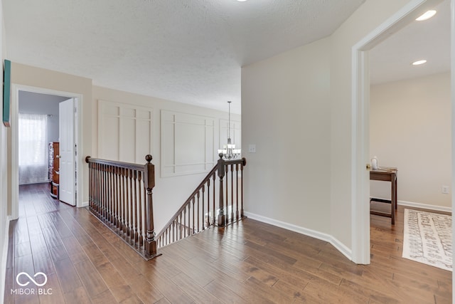 corridor featuring an inviting chandelier, hardwood / wood-style flooring, and a textured ceiling