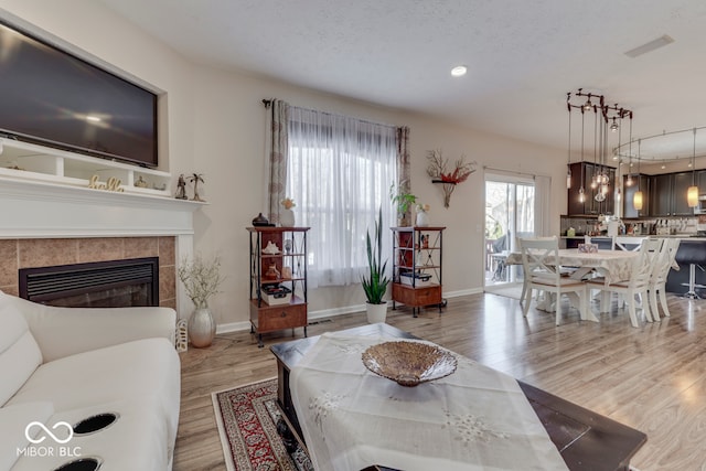 living room featuring a textured ceiling, a tile fireplace, and light hardwood / wood-style flooring