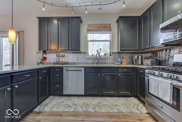 kitchen with appliances with stainless steel finishes, pendant lighting, tasteful backsplash, sink, and light stone countertops