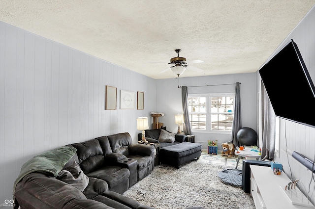 living room featuring a textured ceiling, ceiling fan, and wood walls