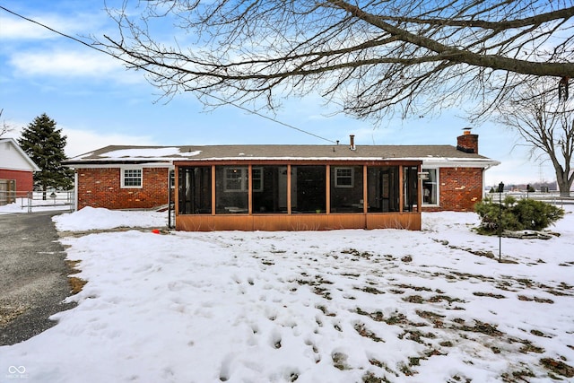 snow covered back of property featuring a sunroom