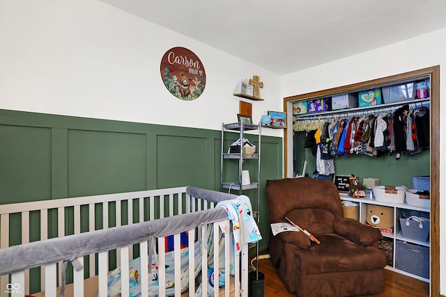 bedroom with a nursery area, dark hardwood / wood-style flooring, and a closet