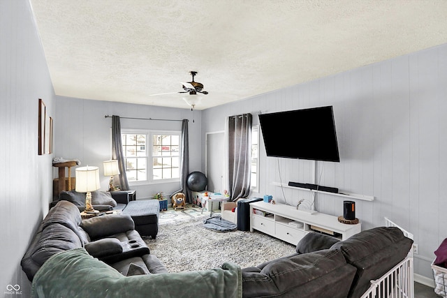 living room featuring ceiling fan, a textured ceiling, and wood walls