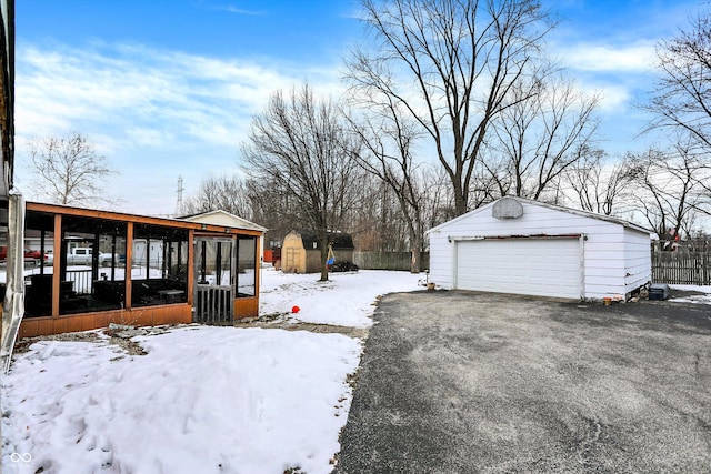 yard layered in snow featuring a shed, a garage, and a sunroom