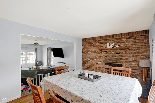 dining area featuring ceiling fan, brick wall, light hardwood / wood-style floors, and a brick fireplace