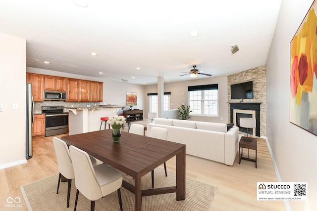 dining area featuring ceiling fan, light hardwood / wood-style flooring, and a fireplace