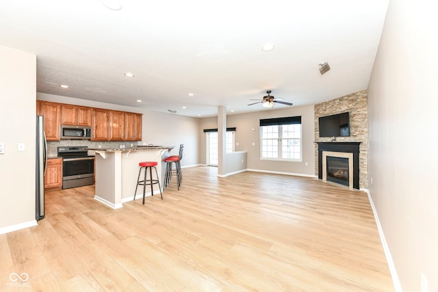 kitchen with open floor plan, a kitchen bar, brown cabinets, stainless steel appliances, and a ceiling fan