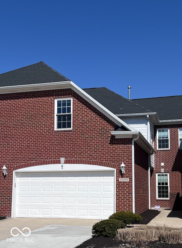 view of front of property featuring brick siding, a garage, driveway, and a shingled roof