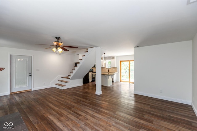 unfurnished living room featuring ceiling fan, dark wood-style flooring, stairway, and baseboards