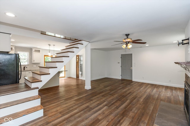 unfurnished living room with dark wood-style flooring, a fireplace, a sink, and stairs