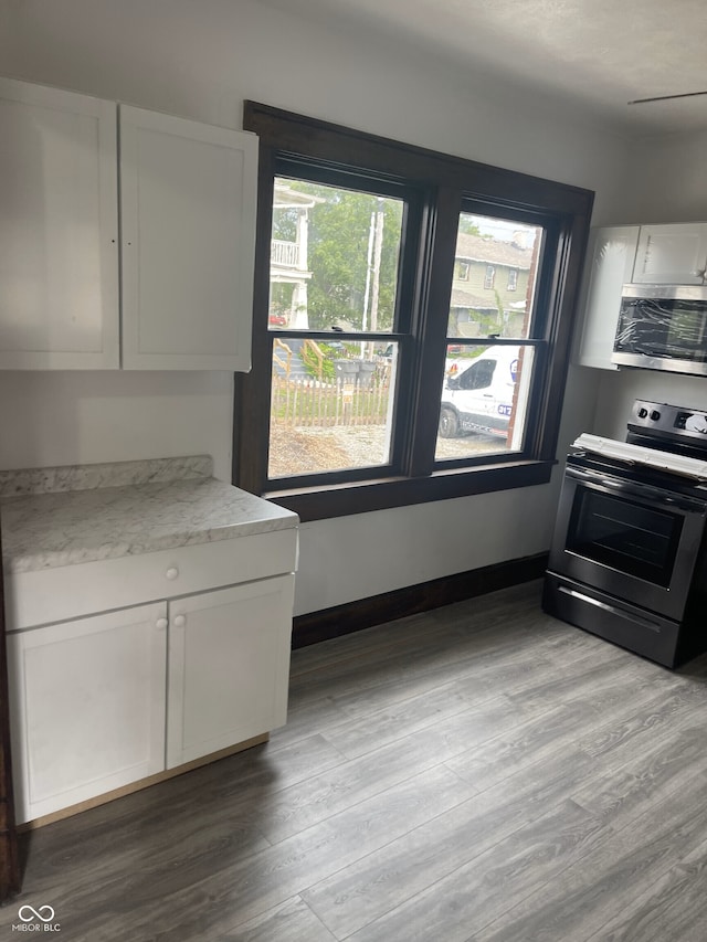 kitchen featuring white cabinetry, light stone countertops, stainless steel appliances, and light wood-type flooring