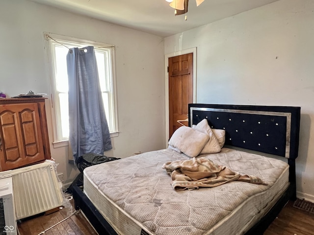 bedroom featuring multiple windows, radiator heating unit, and dark wood-type flooring