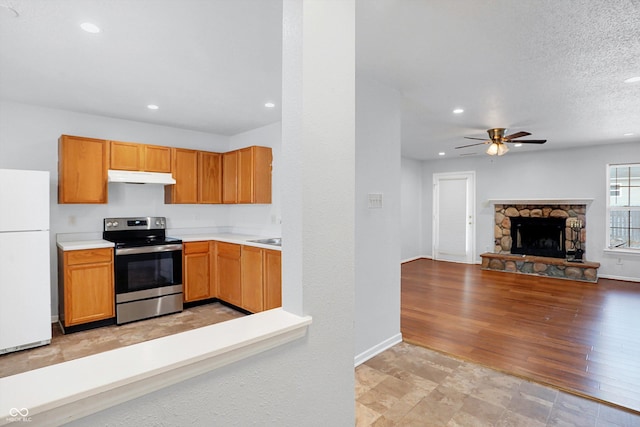 kitchen featuring ceiling fan, white refrigerator, a stone fireplace, electric stove, and a textured ceiling