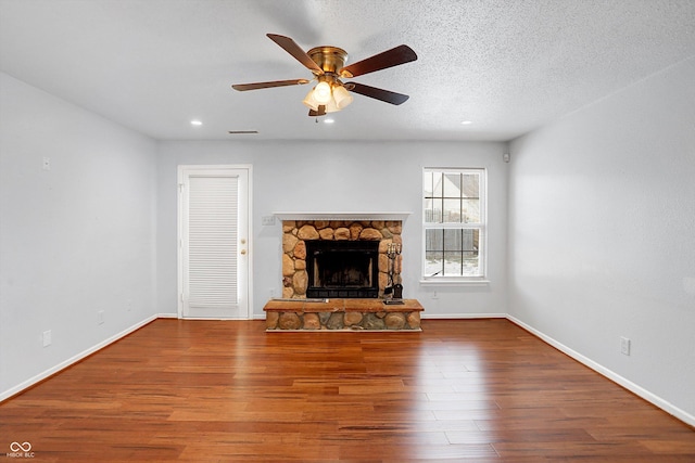 unfurnished living room featuring ceiling fan, hardwood / wood-style flooring, a textured ceiling, and a stone fireplace