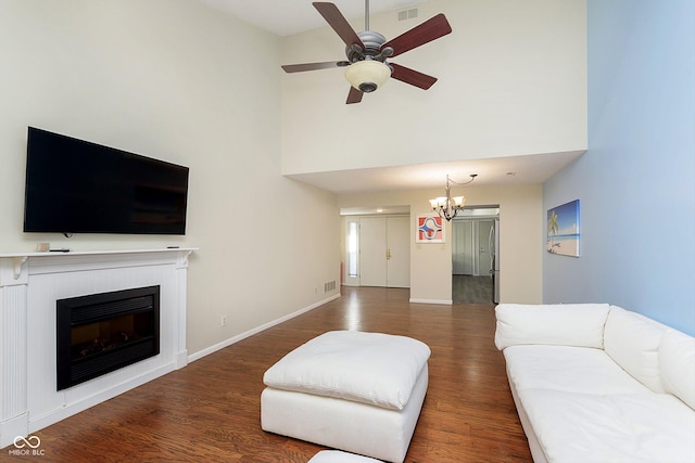 living room with dark hardwood / wood-style flooring, ceiling fan with notable chandelier, and a towering ceiling