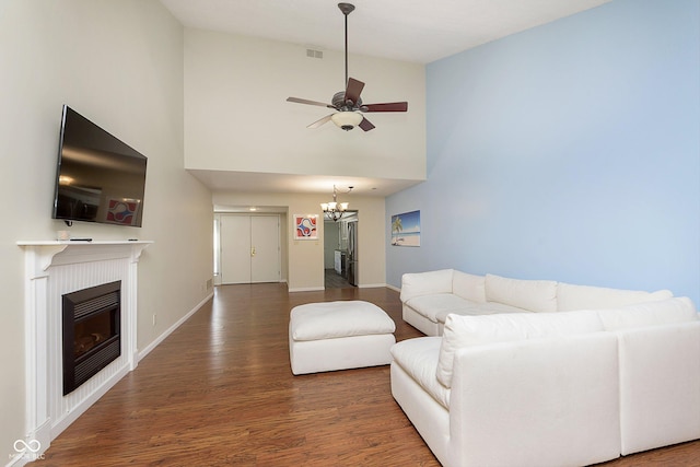 living room featuring dark hardwood / wood-style floors, ceiling fan with notable chandelier, and a towering ceiling