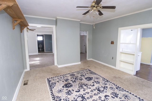 empty room with built in shelves, ceiling fan, crown molding, and carpet floors