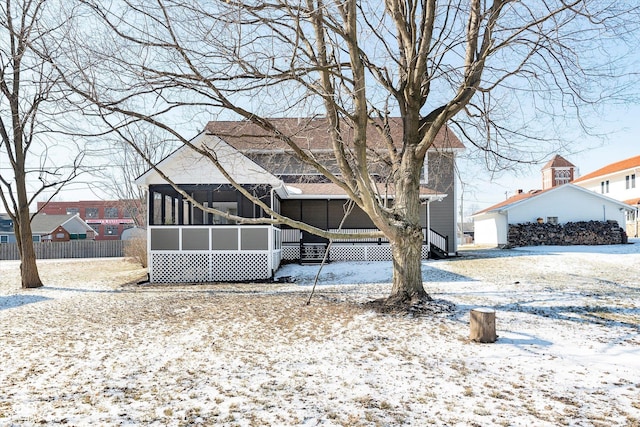 snow covered back of property featuring a sunroom