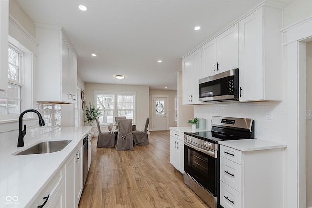 kitchen with sink, white cabinetry, light hardwood / wood-style flooring, stainless steel appliances, and decorative backsplash