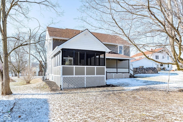 snow covered rear of property featuring a sunroom