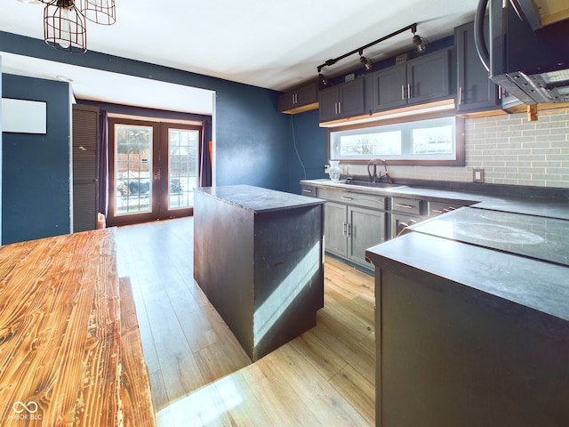 kitchen with french doors, sink, tasteful backsplash, light wood-type flooring, and a kitchen island