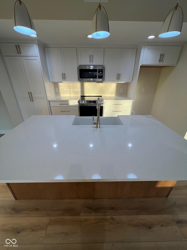 kitchen featuring appliances with stainless steel finishes, decorative light fixtures, white cabinetry, sink, and light wood-type flooring