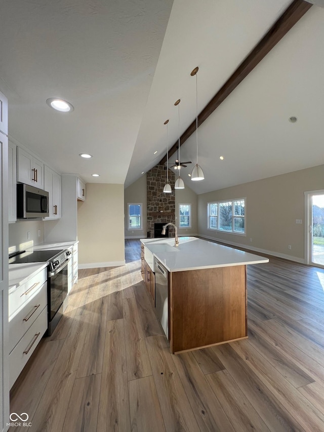 kitchen featuring white cabinetry, vaulted ceiling with beams, a kitchen island with sink, light hardwood / wood-style floors, and stainless steel appliances