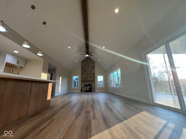 unfurnished living room featuring a stone fireplace, high vaulted ceiling, beamed ceiling, ceiling fan, and light hardwood / wood-style floors