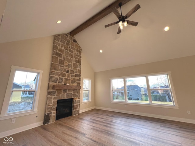 unfurnished living room featuring a healthy amount of sunlight, beam ceiling, and a stone fireplace