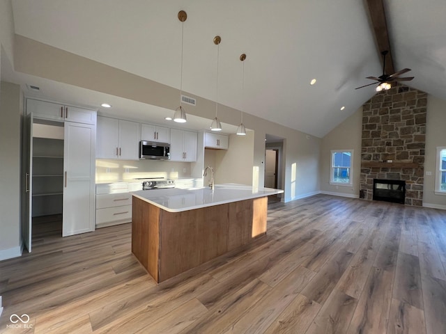 kitchen with white cabinetry, a kitchen island with sink, beamed ceiling, stainless steel appliances, and light hardwood / wood-style floors