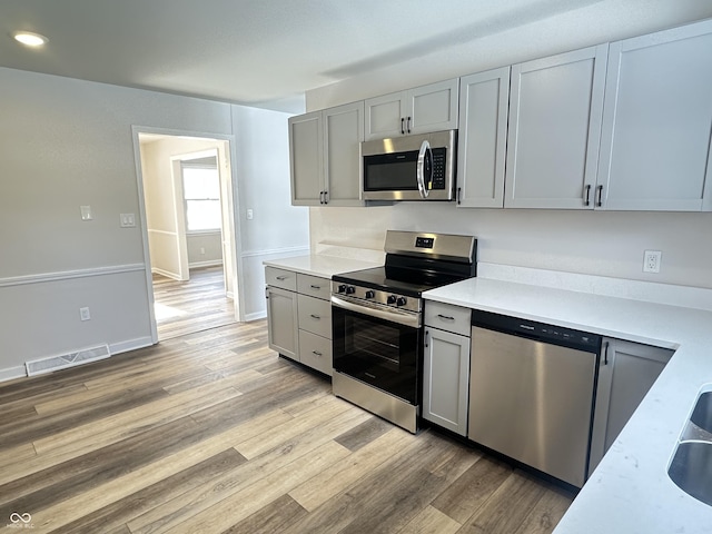 kitchen with stainless steel appliances, gray cabinets, and light wood-type flooring