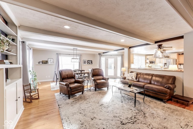 living room with beamed ceiling, ceiling fan, a textured ceiling, and light hardwood / wood-style floors