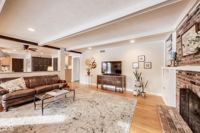 living room with light hardwood / wood-style flooring, beam ceiling, a fireplace, a textured ceiling, and built in shelves