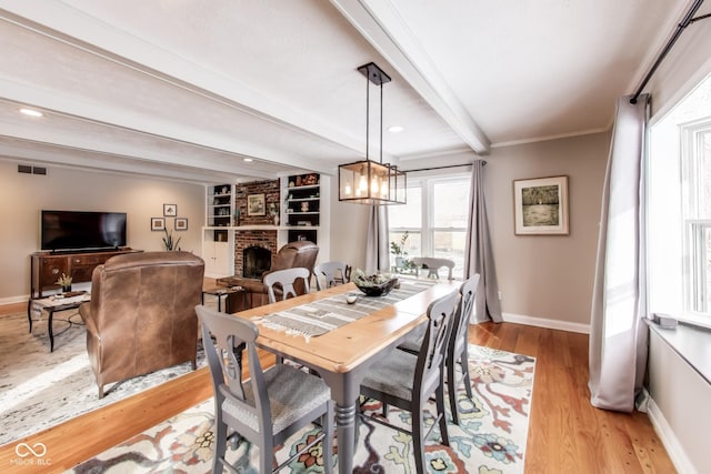 dining area with built in shelves, crown molding, light hardwood / wood-style flooring, beamed ceiling, and a fireplace