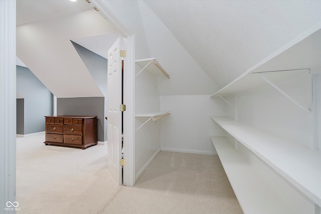 walk in closet with vaulted ceiling and light carpet