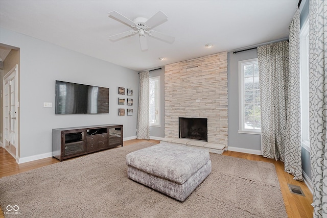 living room featuring hardwood / wood-style flooring, ceiling fan, and a stone fireplace