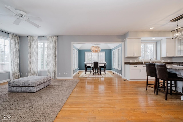 interior space featuring white cabinetry, ceiling fan with notable chandelier, light wood-type flooring, and decorative light fixtures