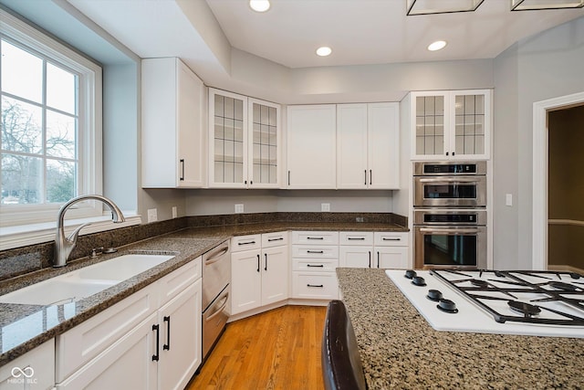 kitchen featuring sink, stone counters, double oven, white gas stovetop, and white cabinets