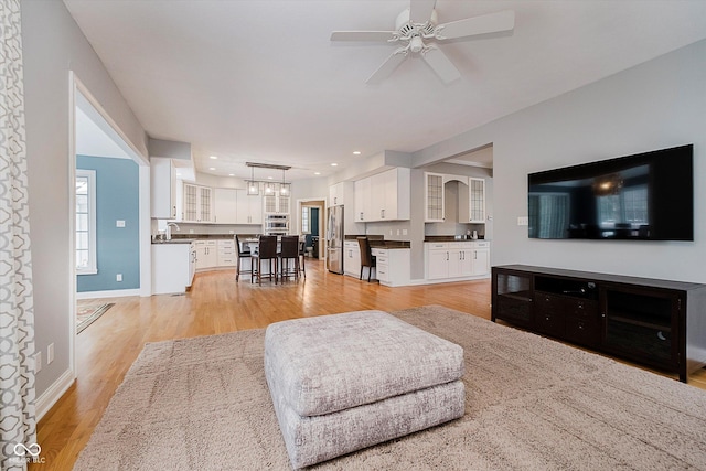 living room featuring ceiling fan, sink, and light wood-type flooring