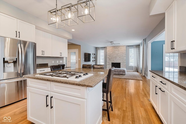 kitchen featuring white gas stovetop, a kitchen island, a breakfast bar area, white cabinets, and stainless steel fridge