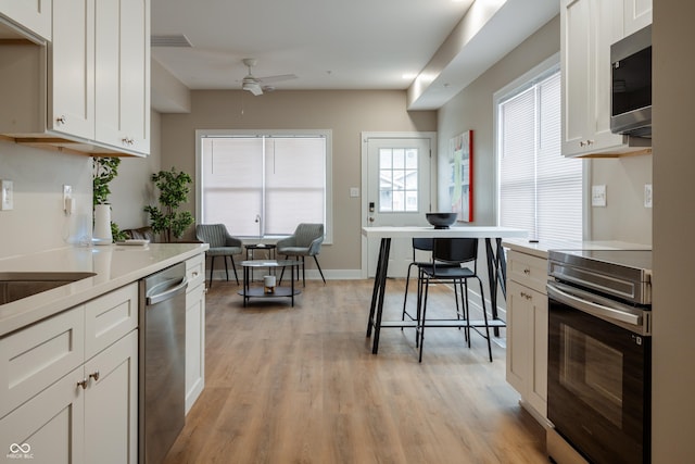 kitchen with stainless steel appliances, ceiling fan, white cabinets, and light wood-type flooring