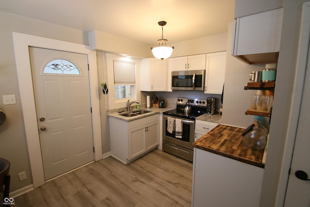 kitchen with appliances with stainless steel finishes, sink, pendant lighting, and white cabinets