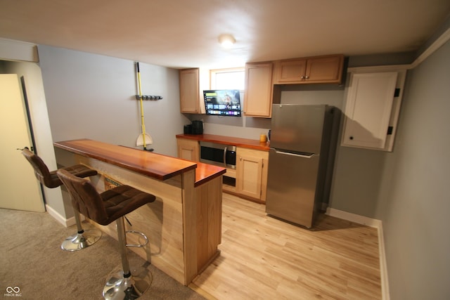 kitchen featuring light hardwood / wood-style floors, appliances with stainless steel finishes, light brown cabinetry, and a breakfast bar area