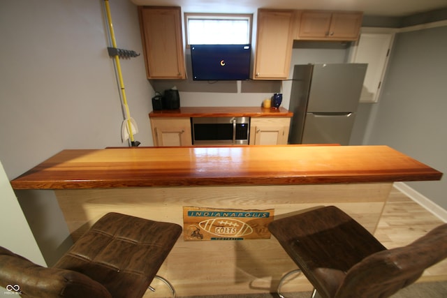 kitchen with wooden counters, light brown cabinetry, stainless steel fridge, and light hardwood / wood-style floors