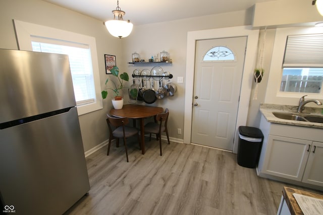 interior space featuring hanging light fixtures, light hardwood / wood-style floors, stainless steel fridge, sink, and white cabinetry