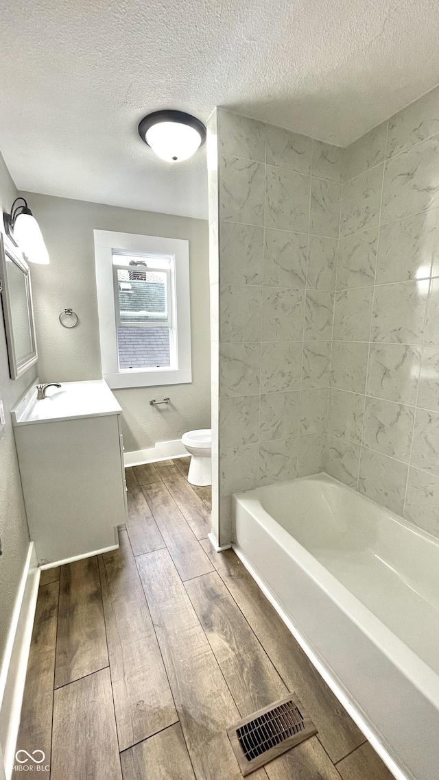 full bathroom featuring vanity, toilet, a textured ceiling, and tiled shower / bath combo