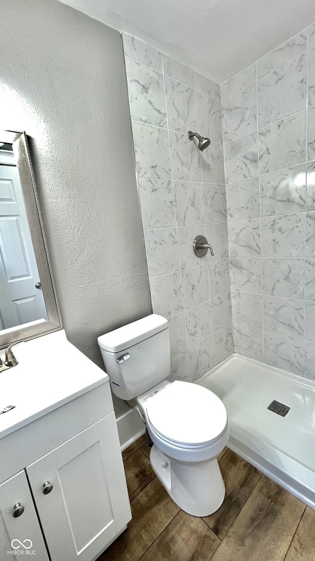 bathroom with a tile shower, toilet, and vanity