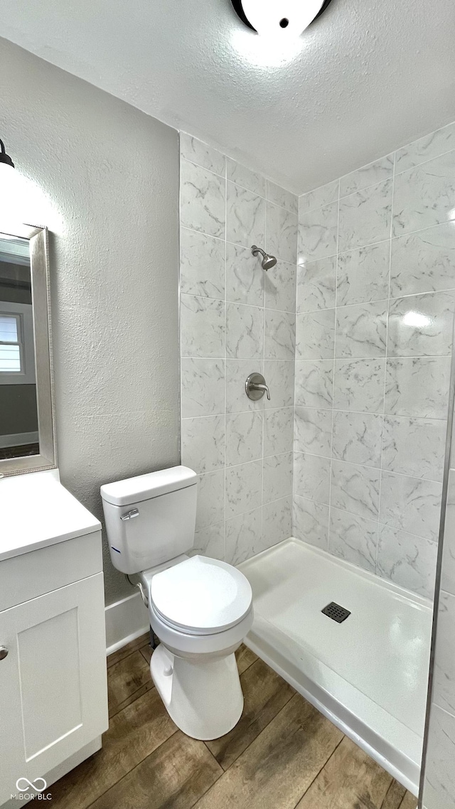 bathroom featuring a textured ceiling, tiled shower, vanity, and toilet