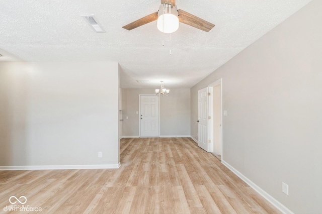 spare room featuring ceiling fan with notable chandelier, light hardwood / wood-style flooring, and a textured ceiling